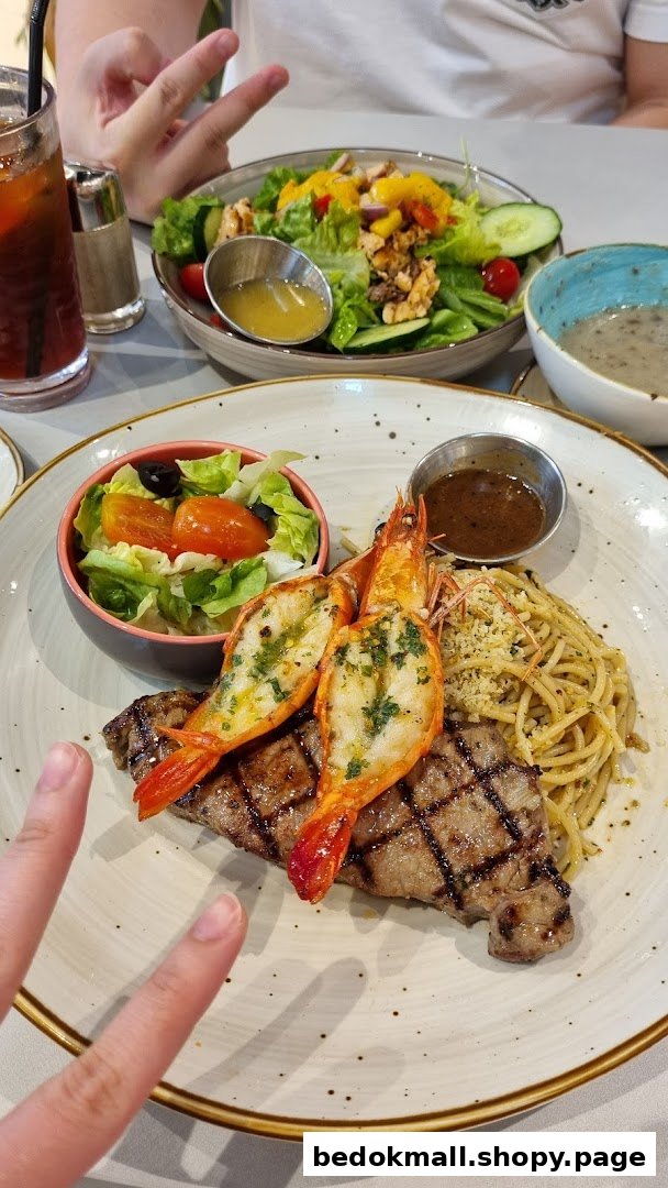 A plate of grilled steak and prawns with pasta and salad on a table.