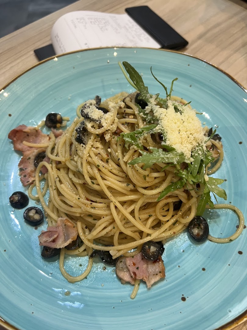 A plate of spaghetti with olives, bacon, cheese, and greens on a blue plate.