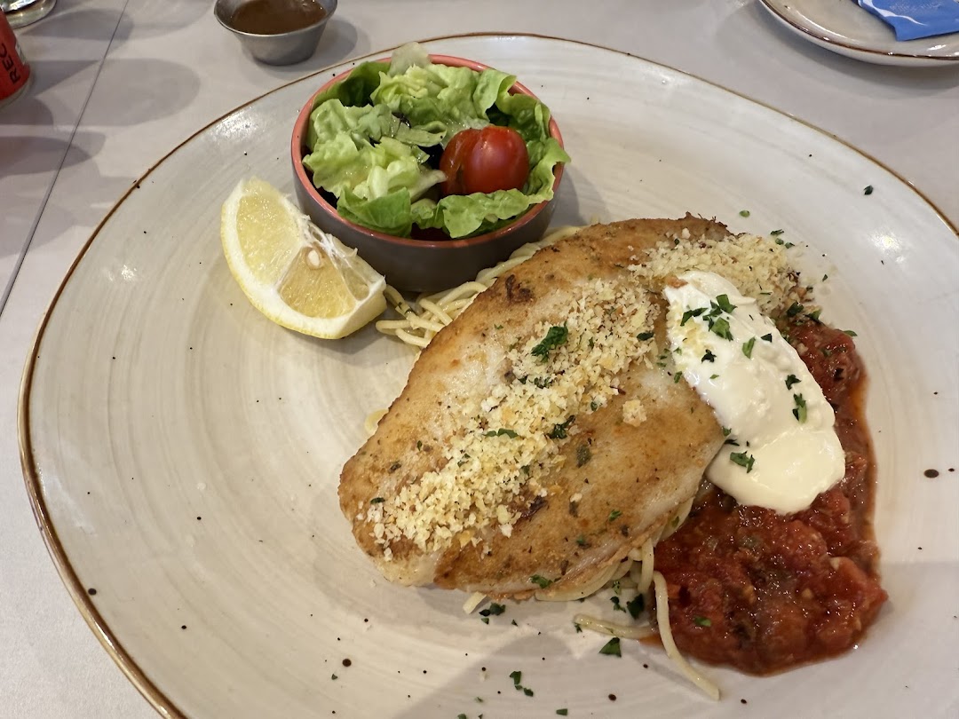 A plate of cooked fish with pasta, tomato sauce, salad, and a lemon wedge.
