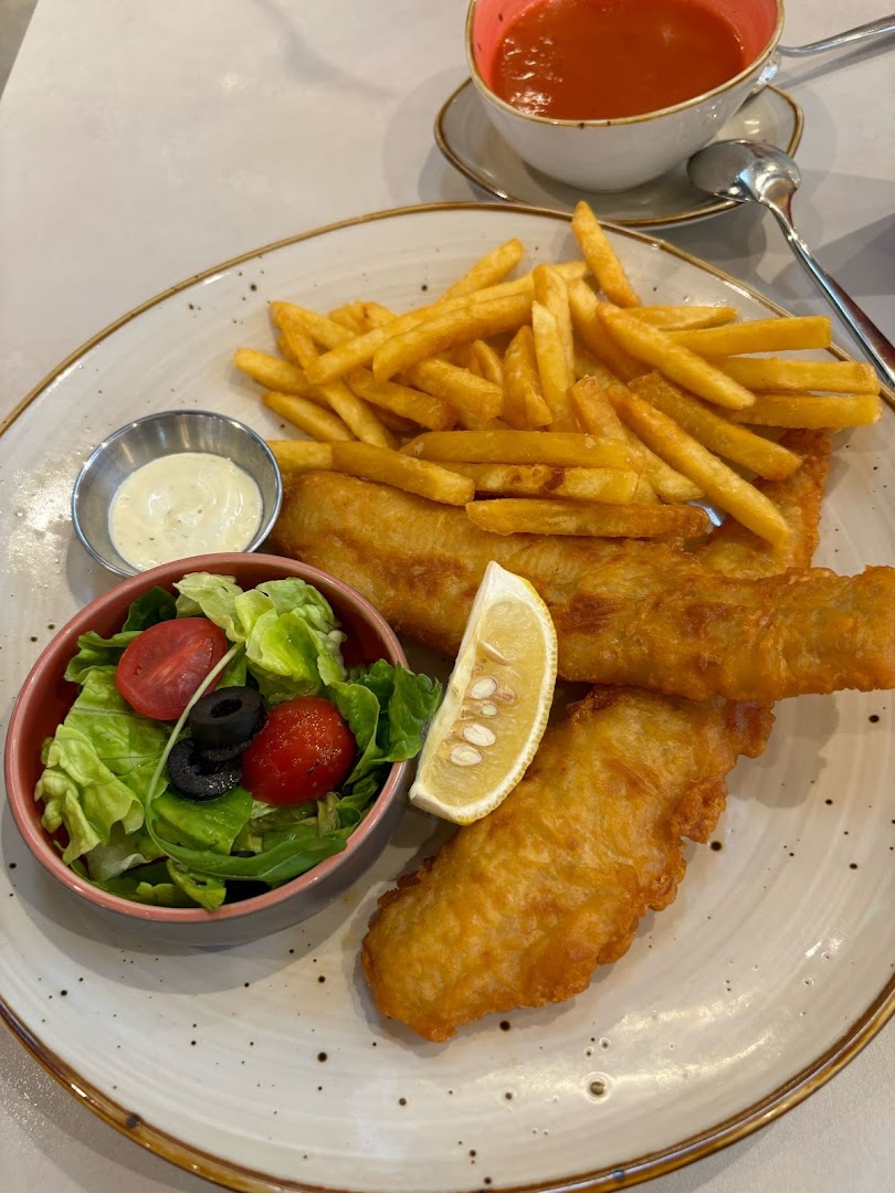 A plate of fish and chips with salad, sauce, and a cup of soup.