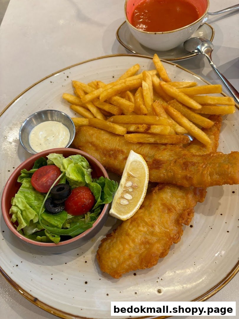 A plate of fish and chips with salad, sauce, and a cup of soup.