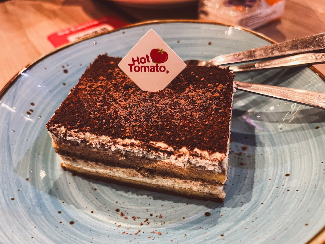 A slice of chocolate-dusted cake with a Hot Tomato pick on a blue plate.