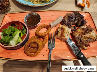 A plate of grilled meats, onion rings, salad, and sauce on a table.