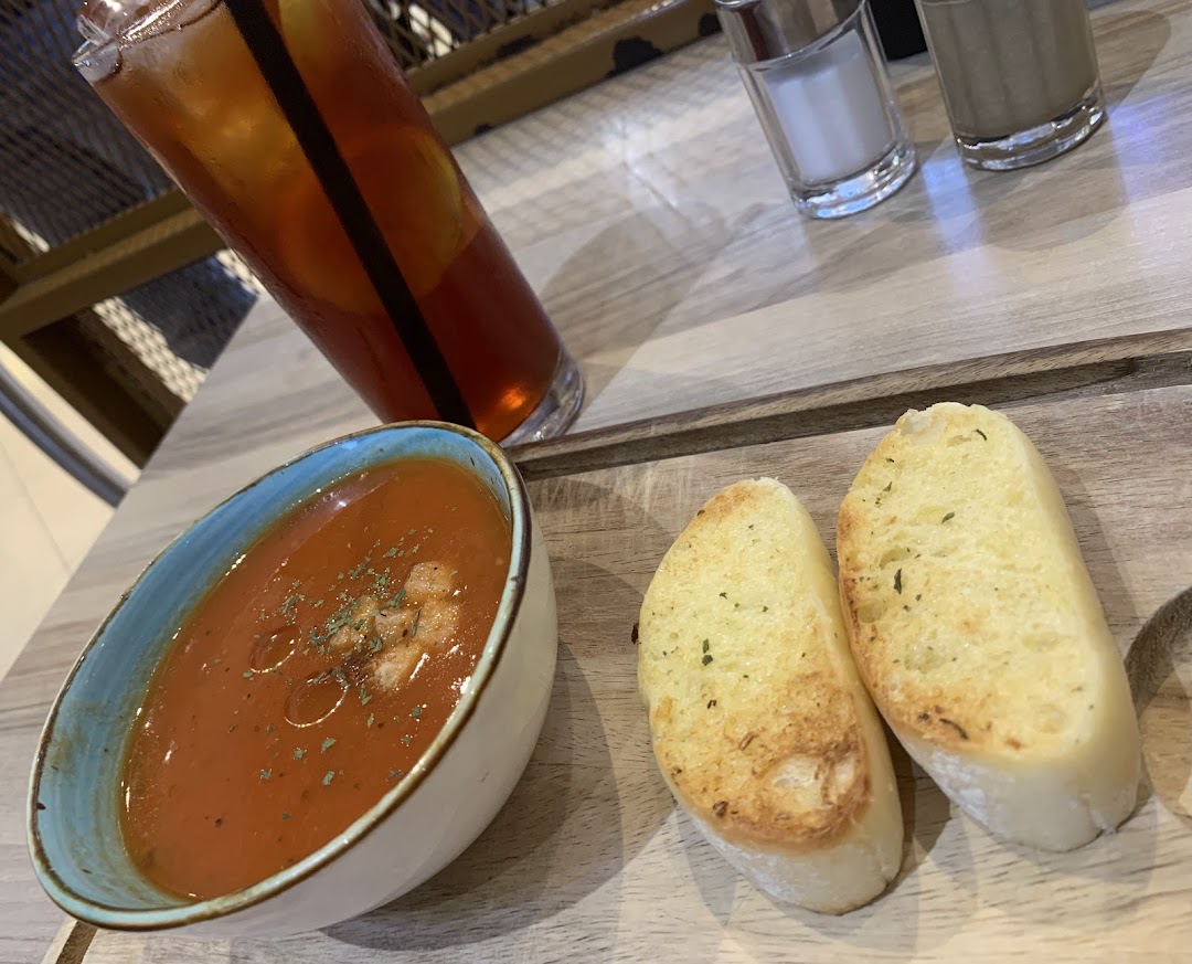A bowl of soup, two bread slices, and an iced tea on a wooden table.