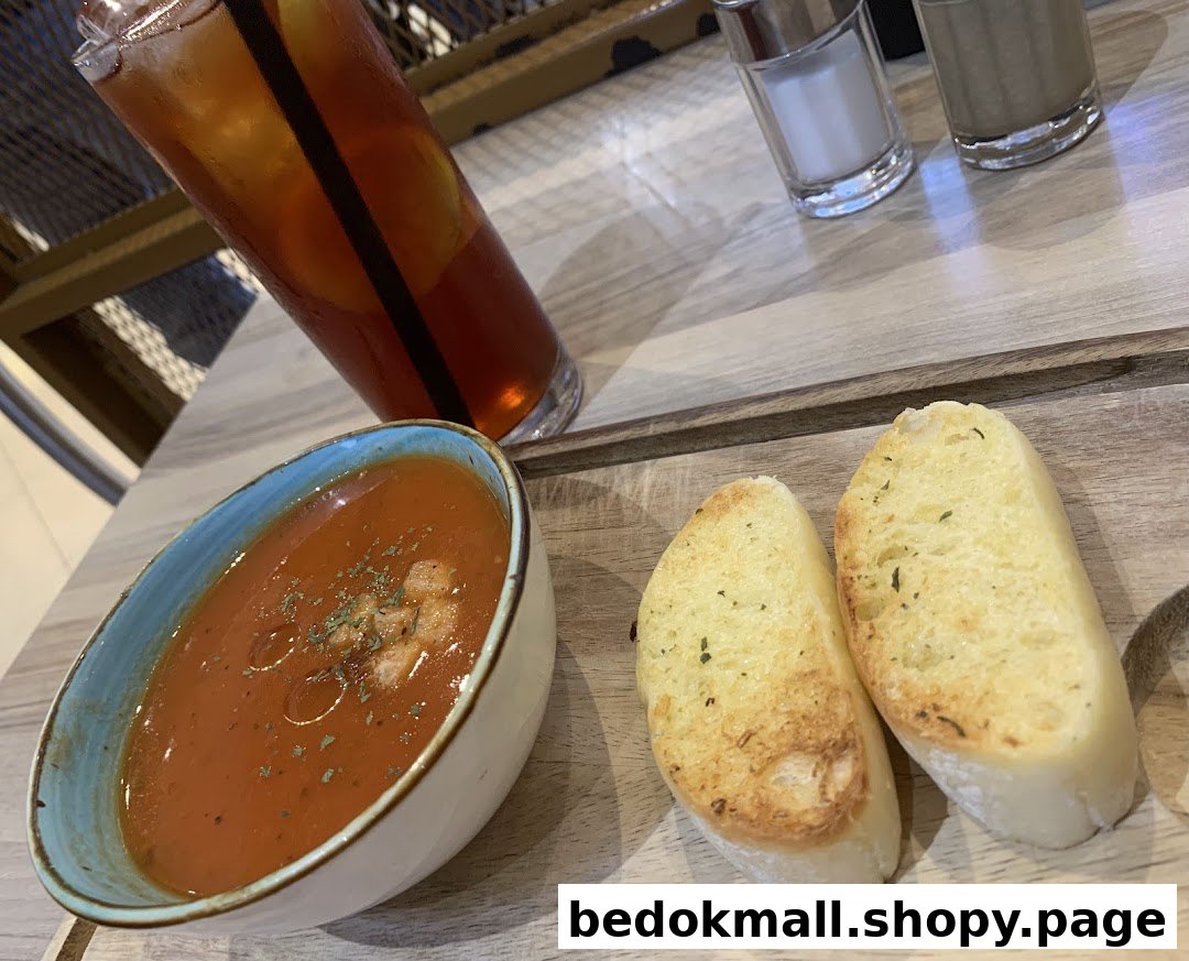 A bowl of soup, two bread slices, and an iced tea on a wooden table.