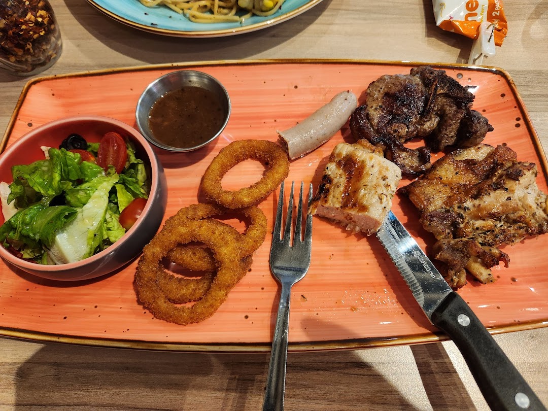 A plate with grilled meats, onion rings, salad, and sauce.