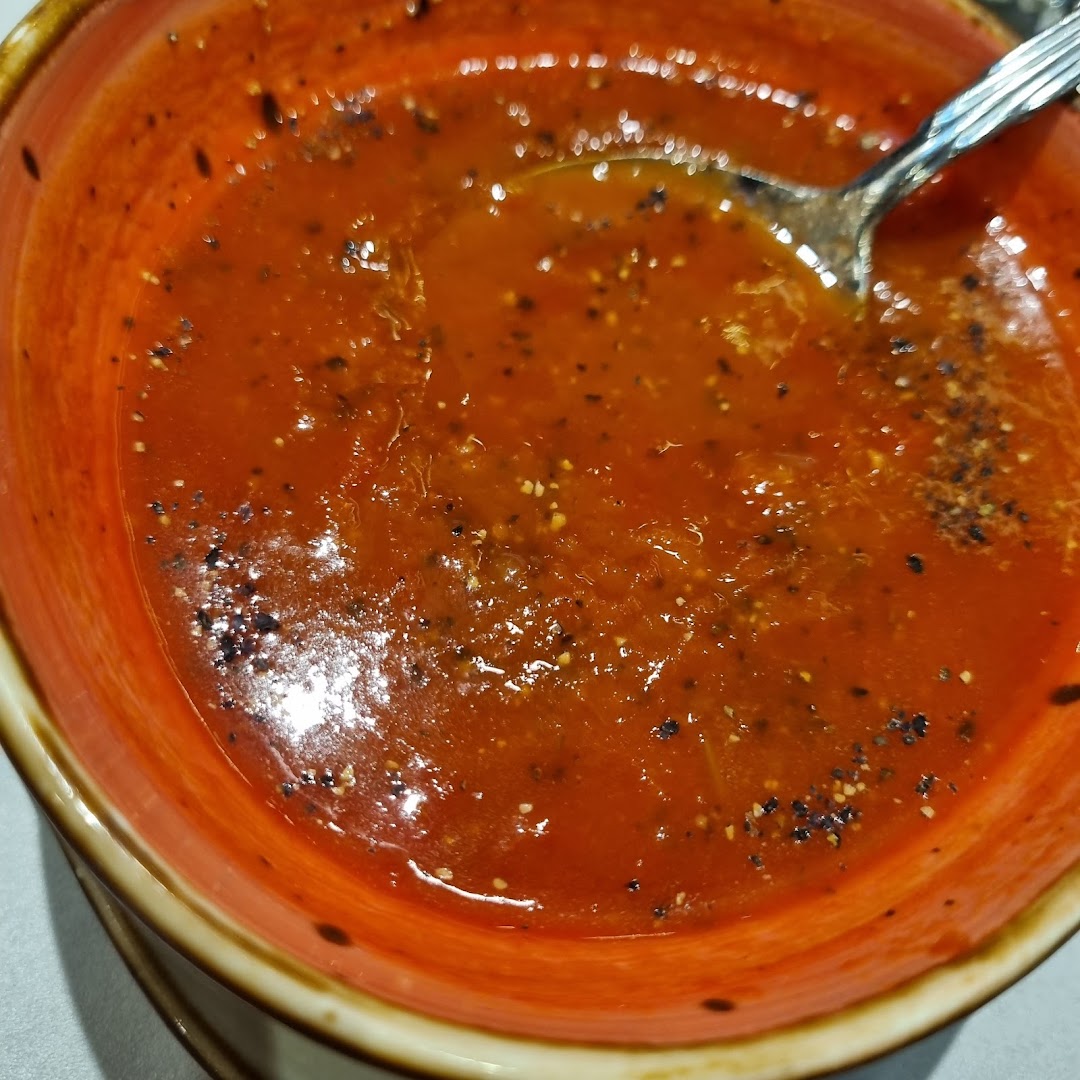 Close-up of a bowl of red soup with a spoon and pepper.