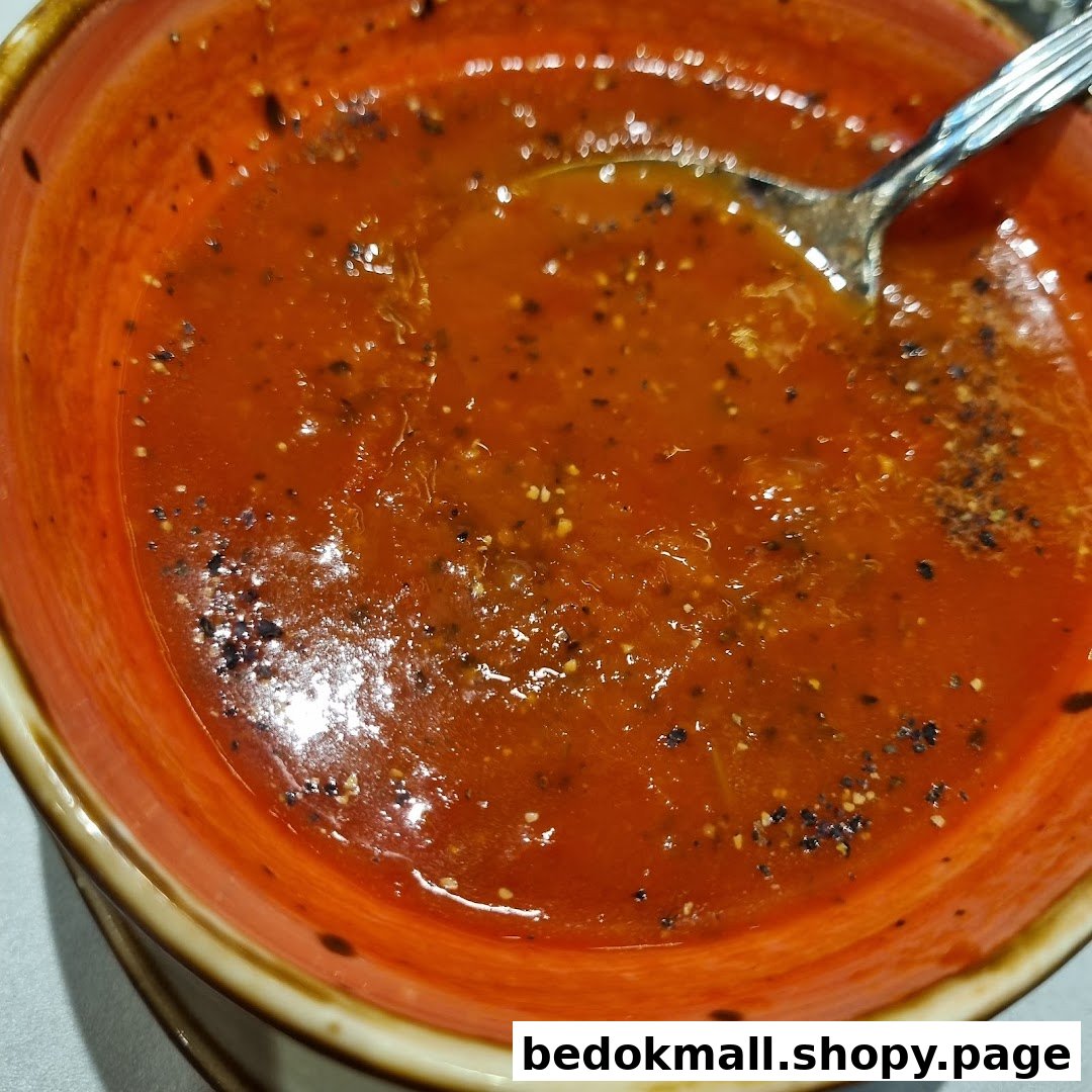 Close-up of a bowl of red soup with a spoon and pepper.
