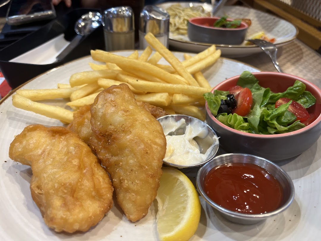 A plate of fish and chips with a side salad and sauces.