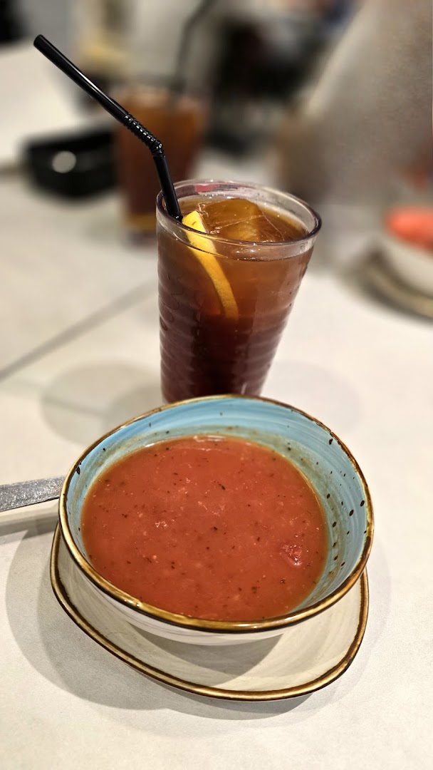 A bowl of tomato soup and a glass of iced tea on a table.