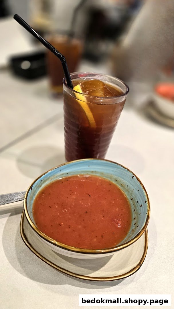 A bowl of tomato soup and a glass of iced tea on a table.