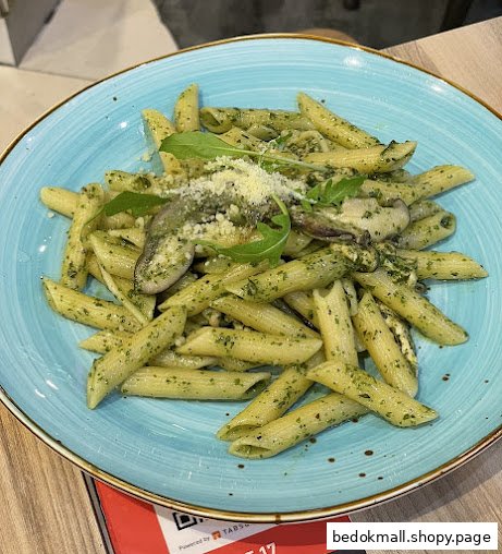 Plate of penne pasta with pesto sauce, mushrooms, and grated cheese.