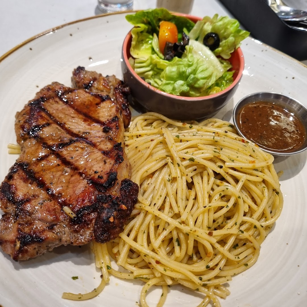 A plate of grilled steak, spaghetti, and a side salad with sauce.
