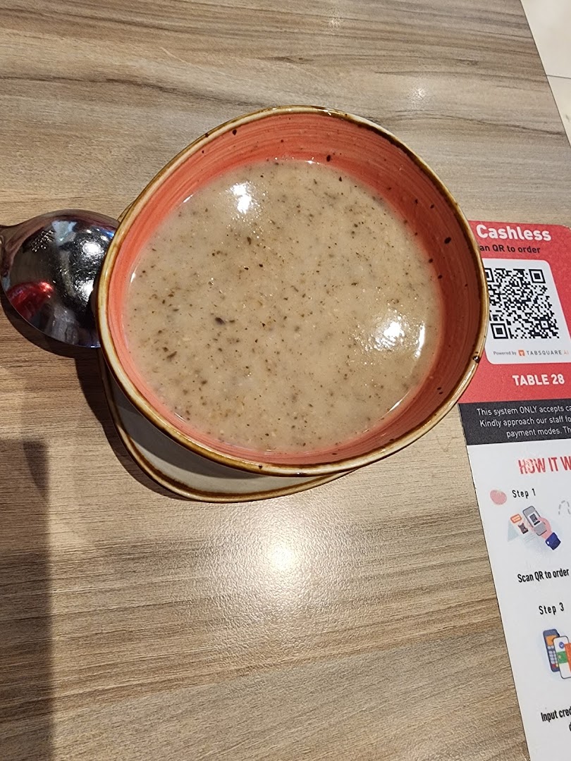 A bowl of soup and a spoon on a wooden table next to a cashless ordering sign.