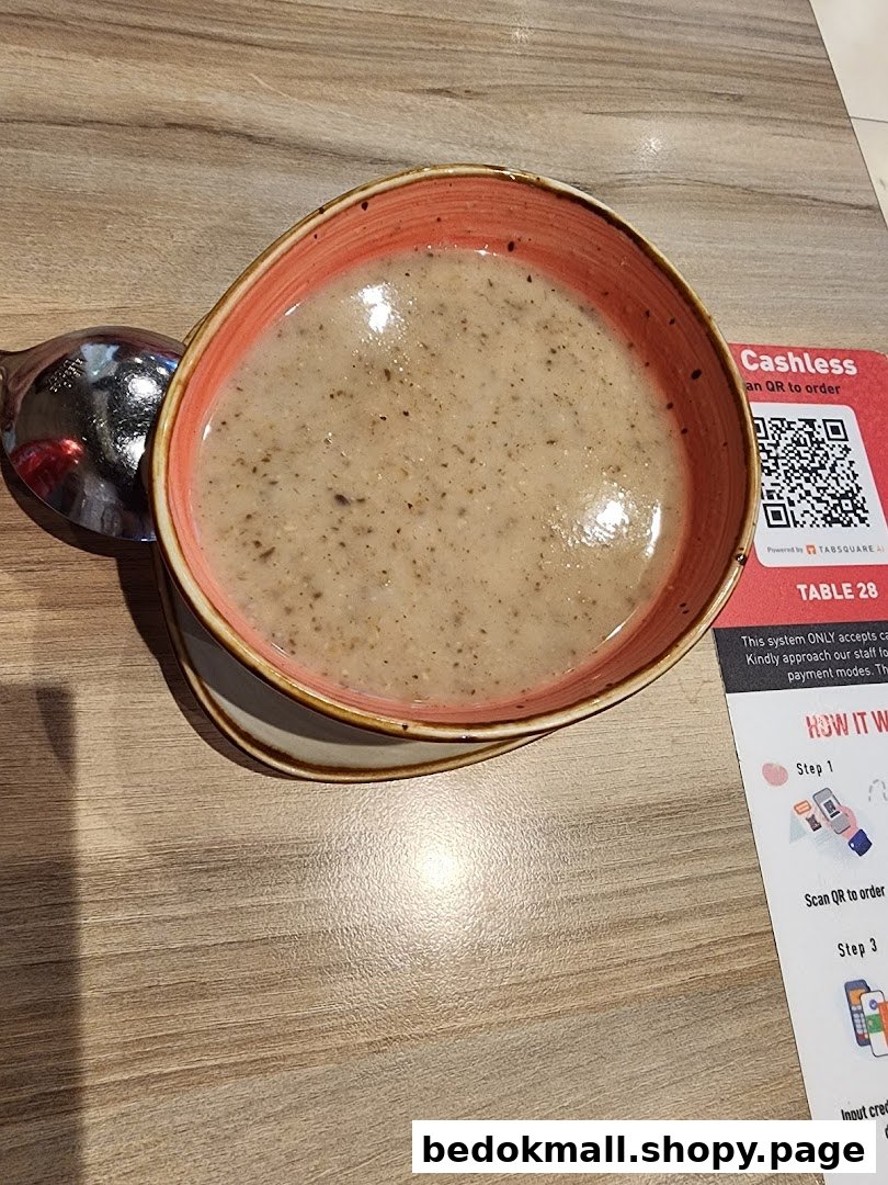 A bowl of soup and a spoon on a wooden table next to a cashless ordering sign.