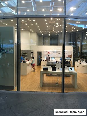 Interior view of an electronics store with display tables, products, and customers.