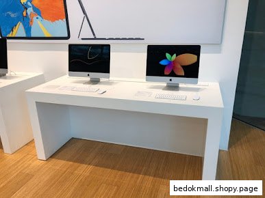 Two iMac computers are displayed on a white table in a retail store.