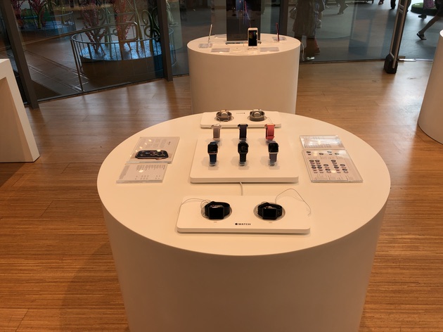 White display tables with smartwatches and phones inside a modern retail store.