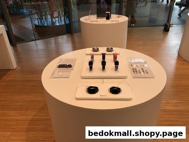 White display tables with smartwatches and phones inside a modern retail store.