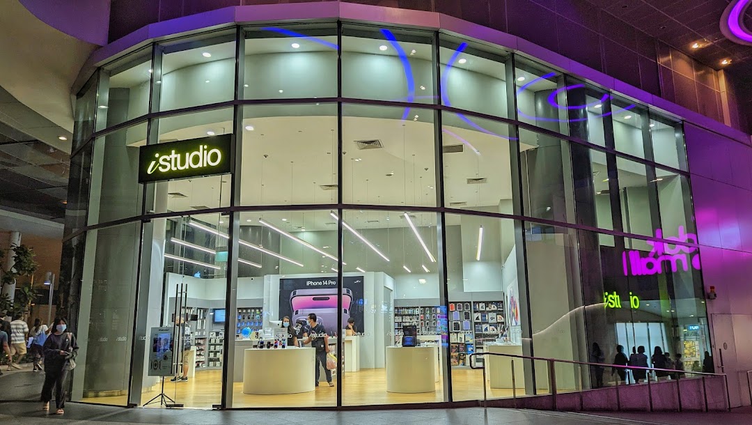Exterior view of iStudio electronics store with large glass windows at night.