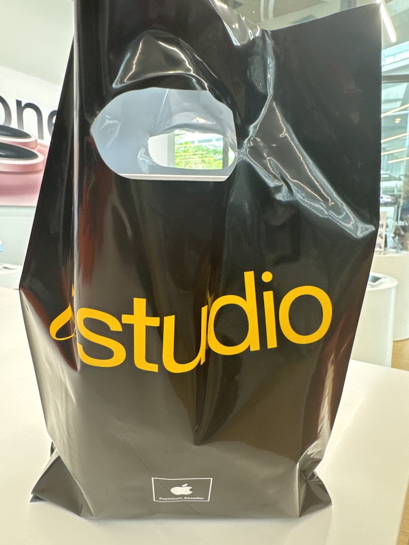 Black iStudio shopping bag with yellow logo on a white table.
