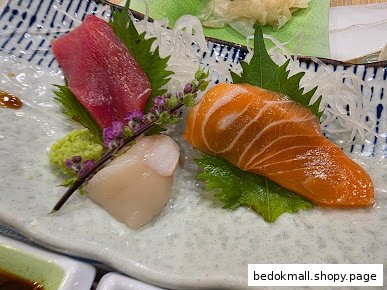 A plate of sashimi with tuna, salmon, and scallop, garnished with wasabi.