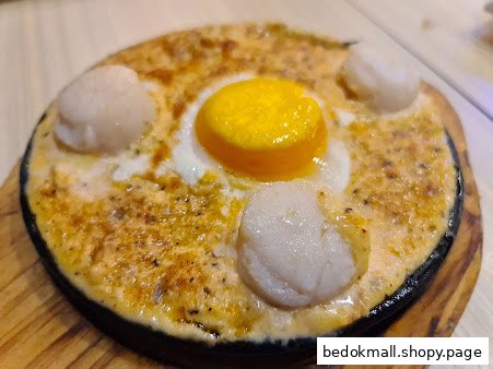 A sizzling plate with an egg yolk and scallops in a creamy sauce.