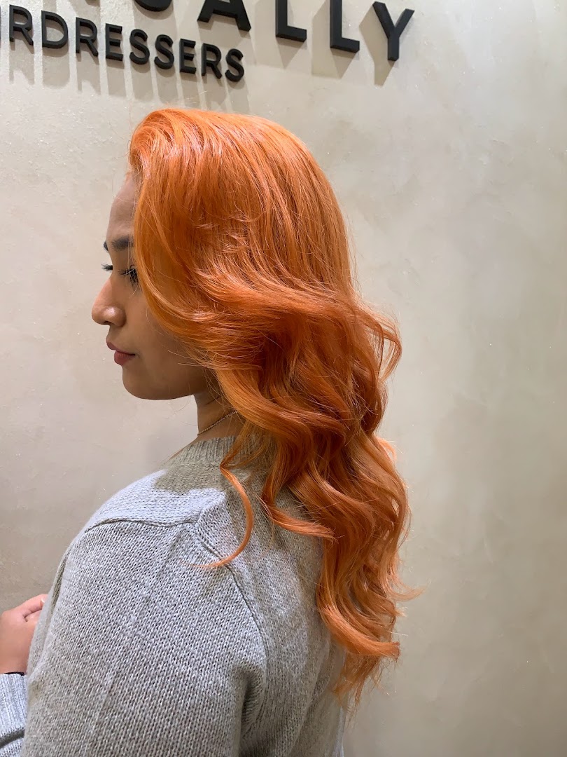 Person with vibrant orange hair in a salon setting, showing a hair service result.