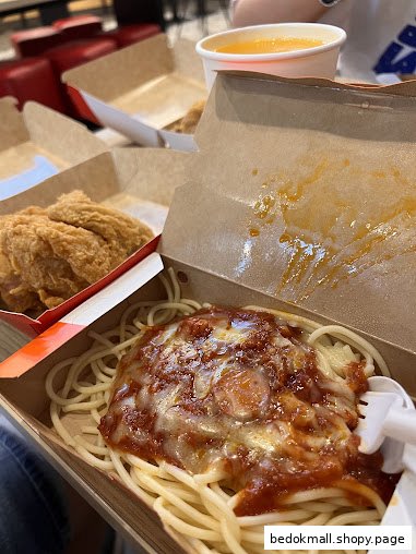 Spaghetti and fried chicken in takeout boxes with a drink on a table.