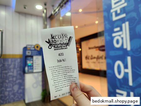 A hand holds a kcuts service ticket in front of the shop's interior.