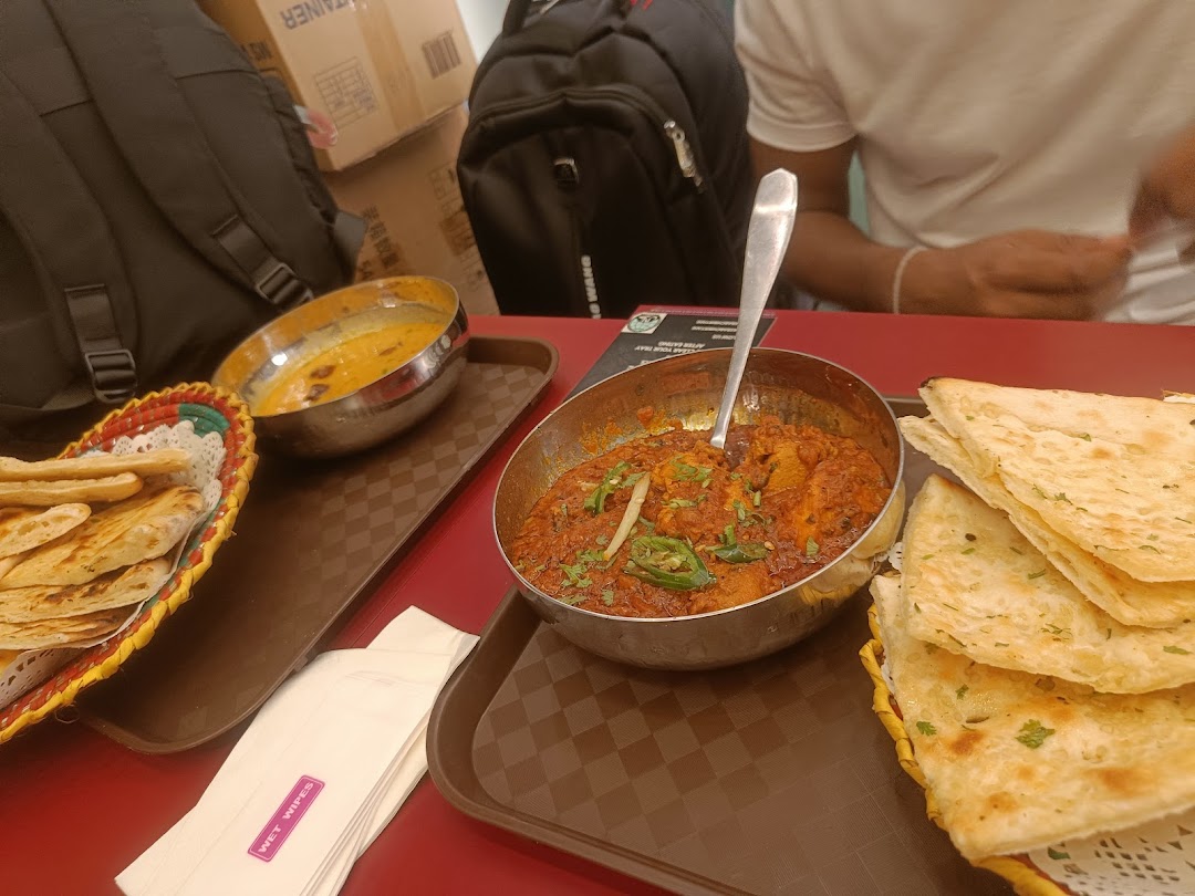 Food on trays at a table with a person and backpacks in the background.
