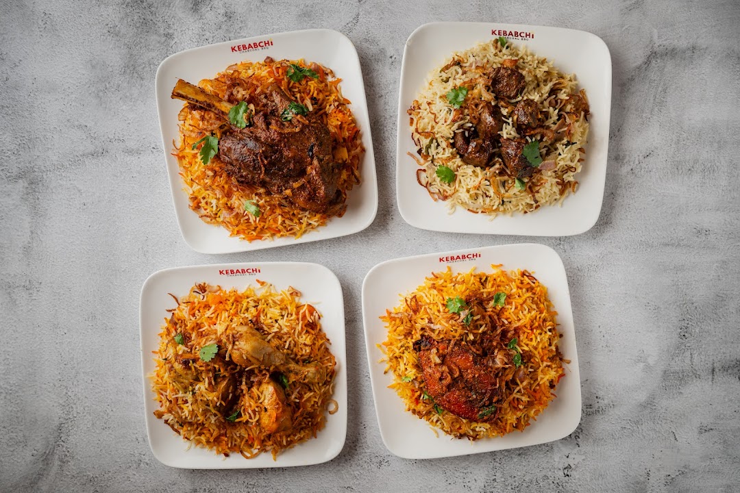 Four plates of biryani with various meats on a grey background.