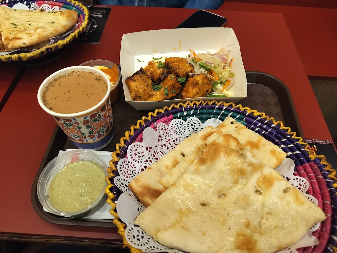 A tray with naan, chicken, tea, and sauces on a red table.