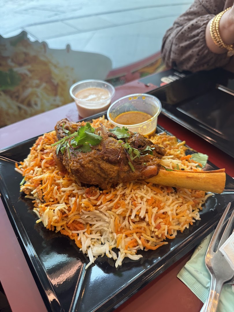 A plate of biryani with a lamb shank and sauces on a table.