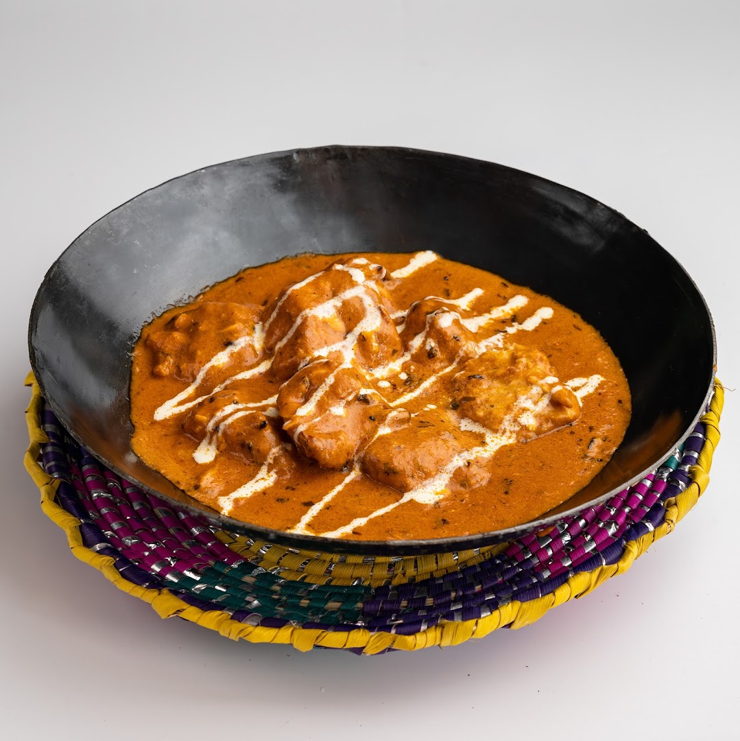 A dish of chicken curry with cream drizzle in a black bowl on a colorful mat.