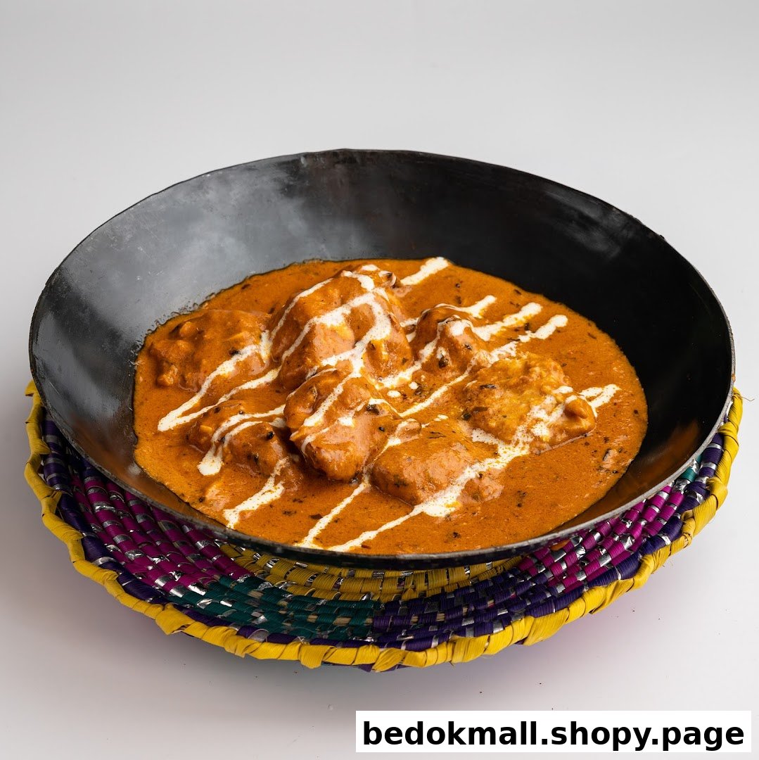 A dish of chicken curry with cream drizzle in a black bowl on a colorful mat.