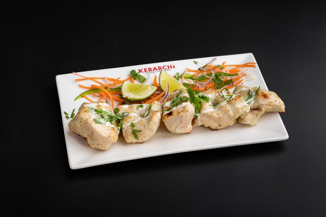 A plate of chicken kebabs with lime, sauce, and shredded vegetables.
