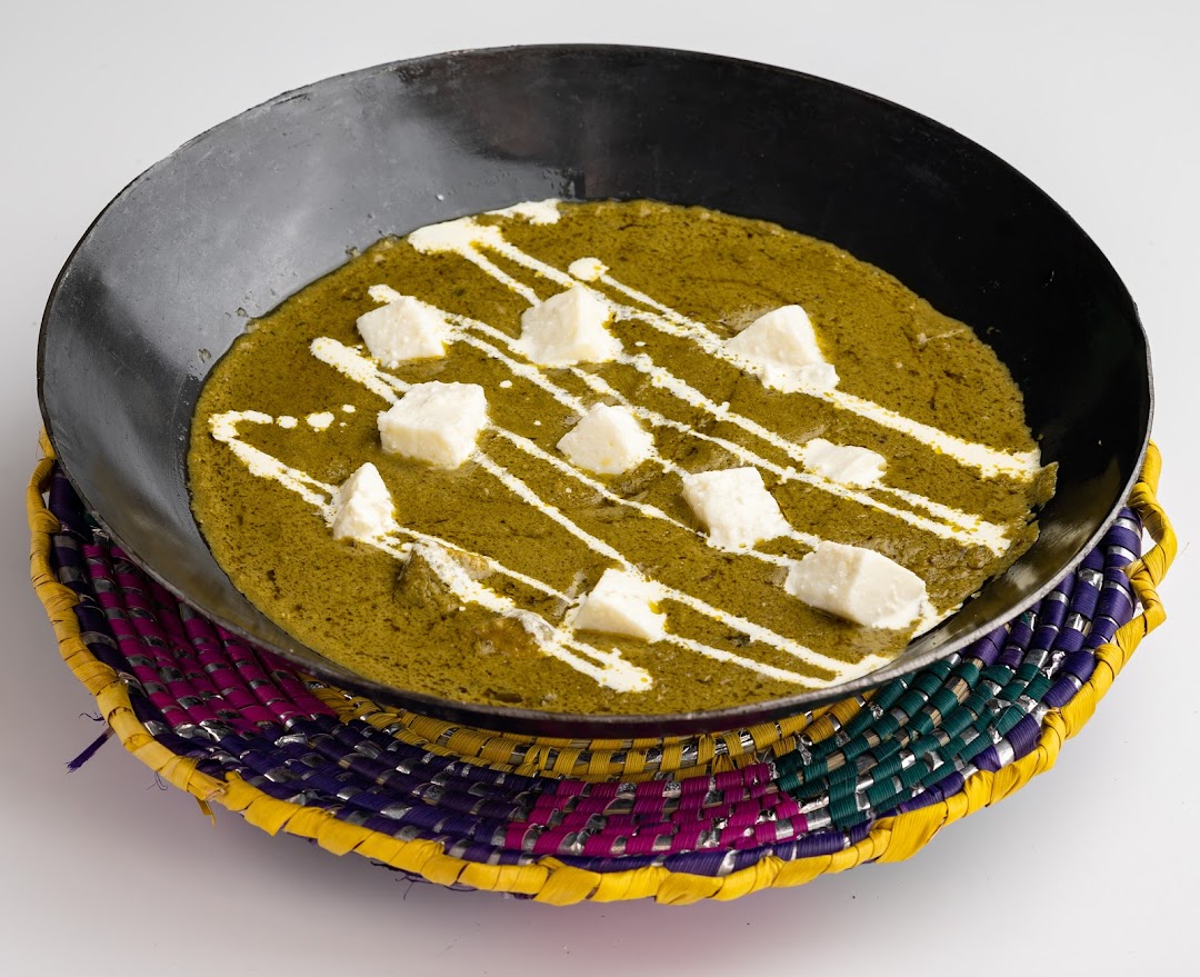 A green curry with paneer and cream in a black pan on a colorful woven mat.