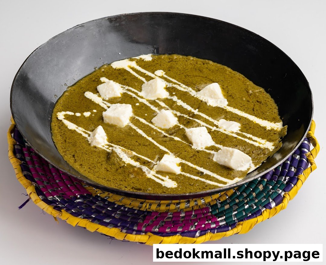 A green curry with paneer and cream in a black pan on a colorful woven mat.