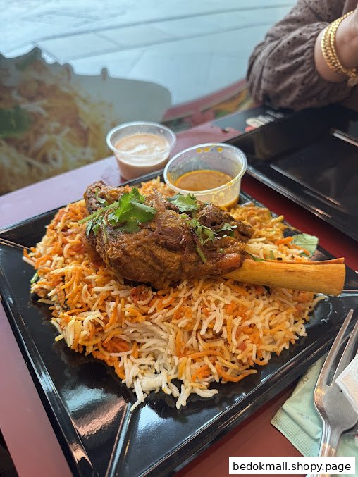 A plate of biryani with a large meat shank and two small sauce cups.