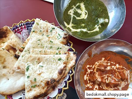 Naan bread and two bowls of curry on a red table.