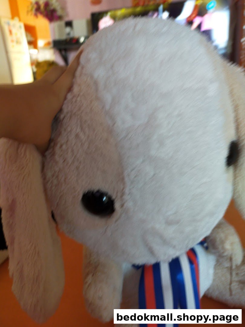 A hand touching a large, light-colored plush toy with a striped ribbon.