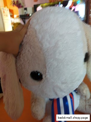 A hand touches a large, white plush toy with a blue, white, and red ribbon.