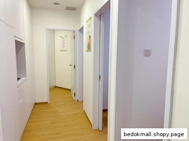 A clean, white interior hallway with multiple doors and wooden flooring.