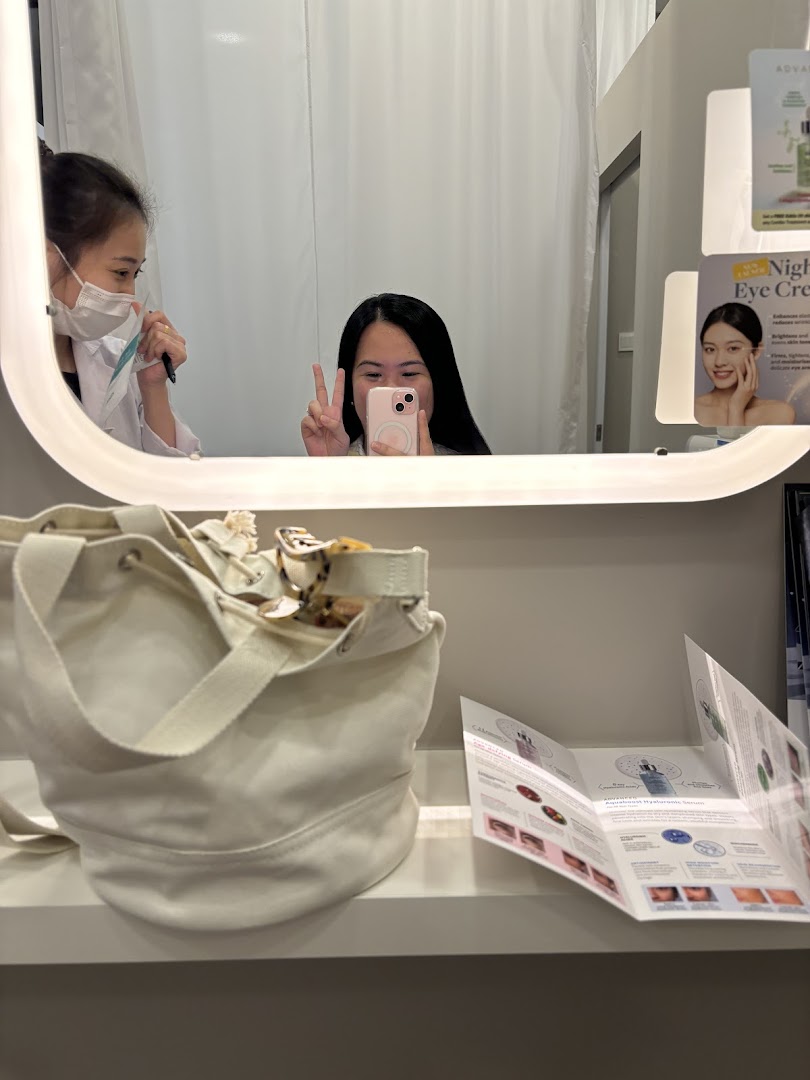 Reflections of two people in a mirror with a bag and brochures on a shelf.