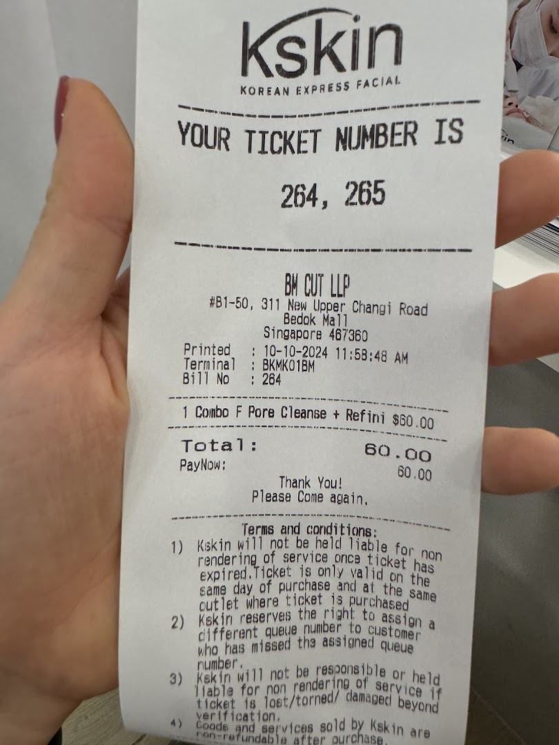 A hand holds a printed receipt for a Kskin Korean Express Facial service.