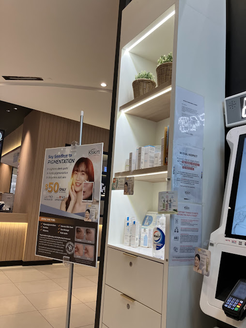 Interior view of a Kskin shop with product display, promotional poster, and kiosk.