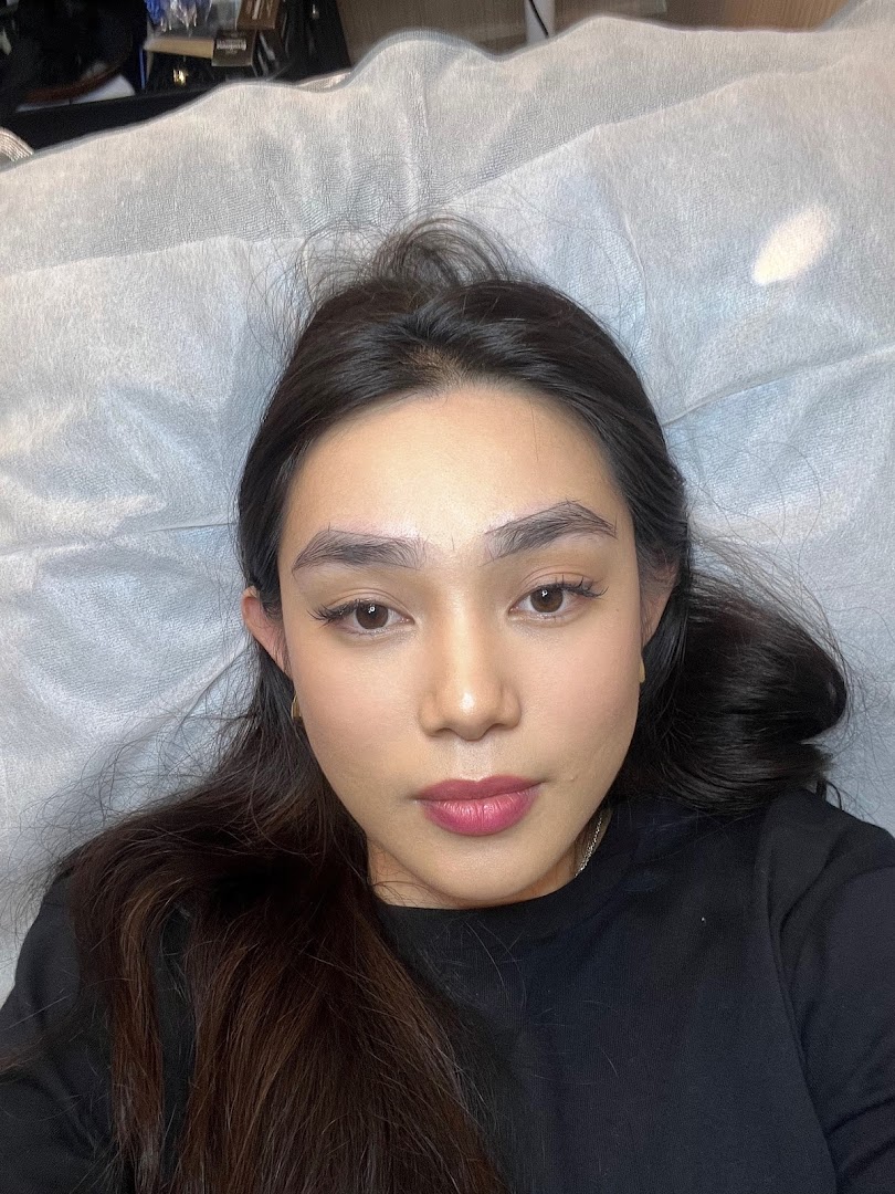 A person lying on a bed, likely receiving an eyebrow treatment.