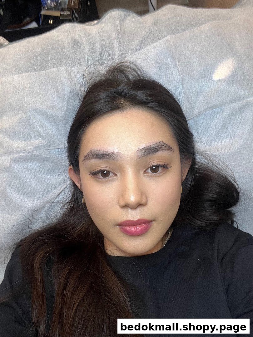 A person lying on a bed, likely receiving an eyebrow treatment.