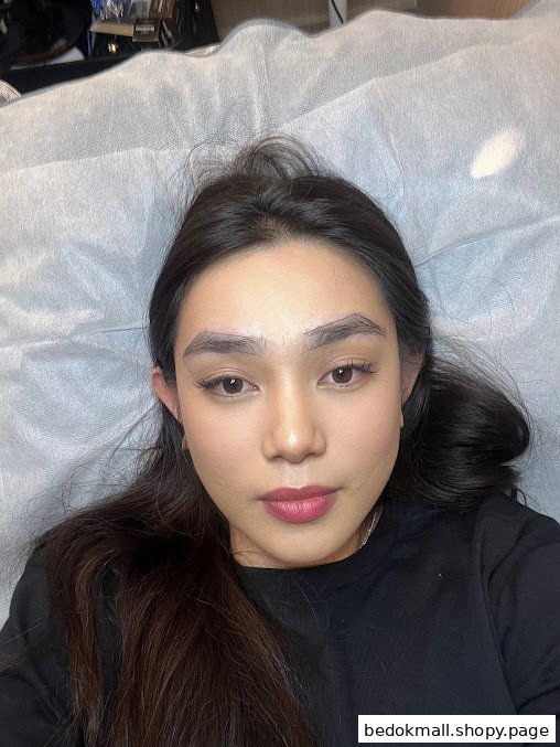 Woman with marked eyebrows lying on a bed, likely for a beauty treatment.